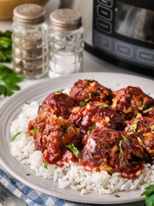 porcupine meatballs with sauce on a plate in from of a crockpot.