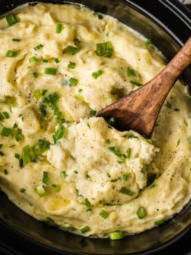 Sour cream and onion mashed potatoes in a slow cooker with a wooden spoon in it.