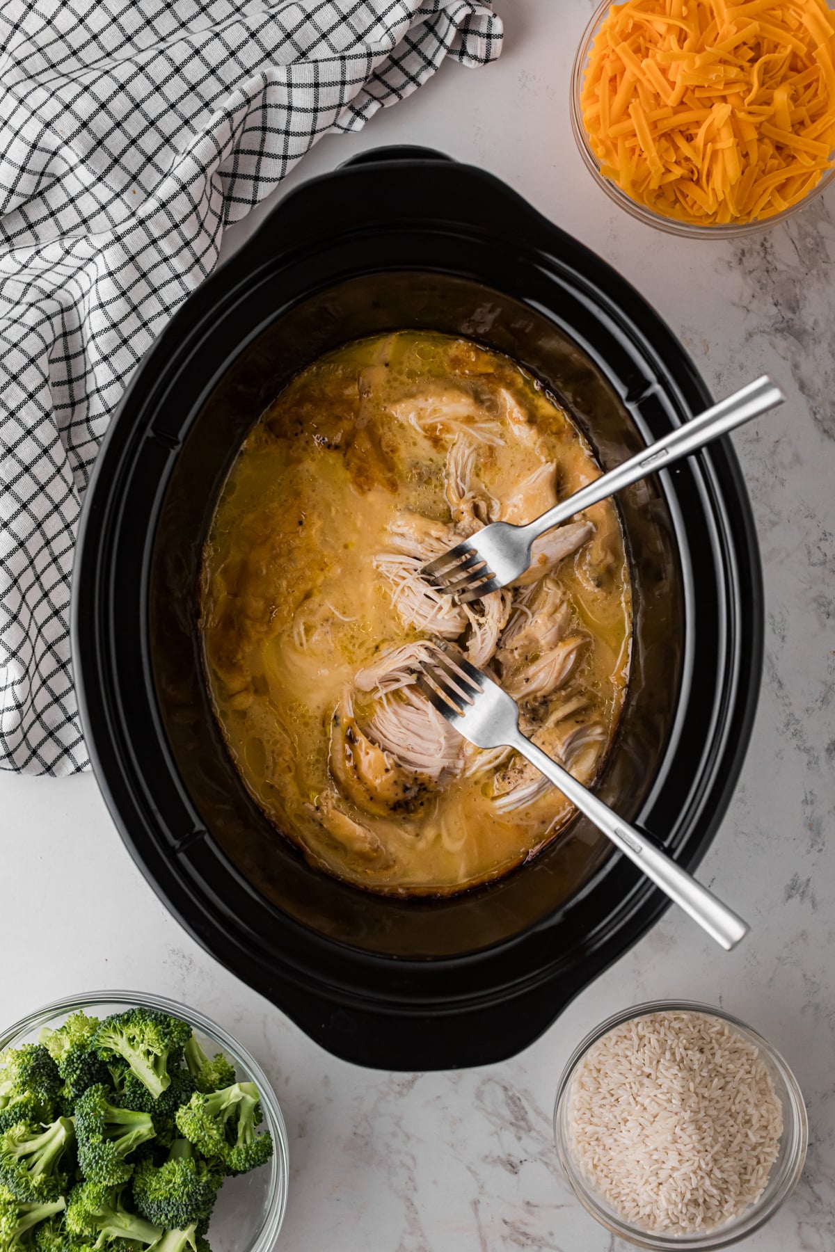 Shredding cooked chicken breasts with two forks in a crockpot.