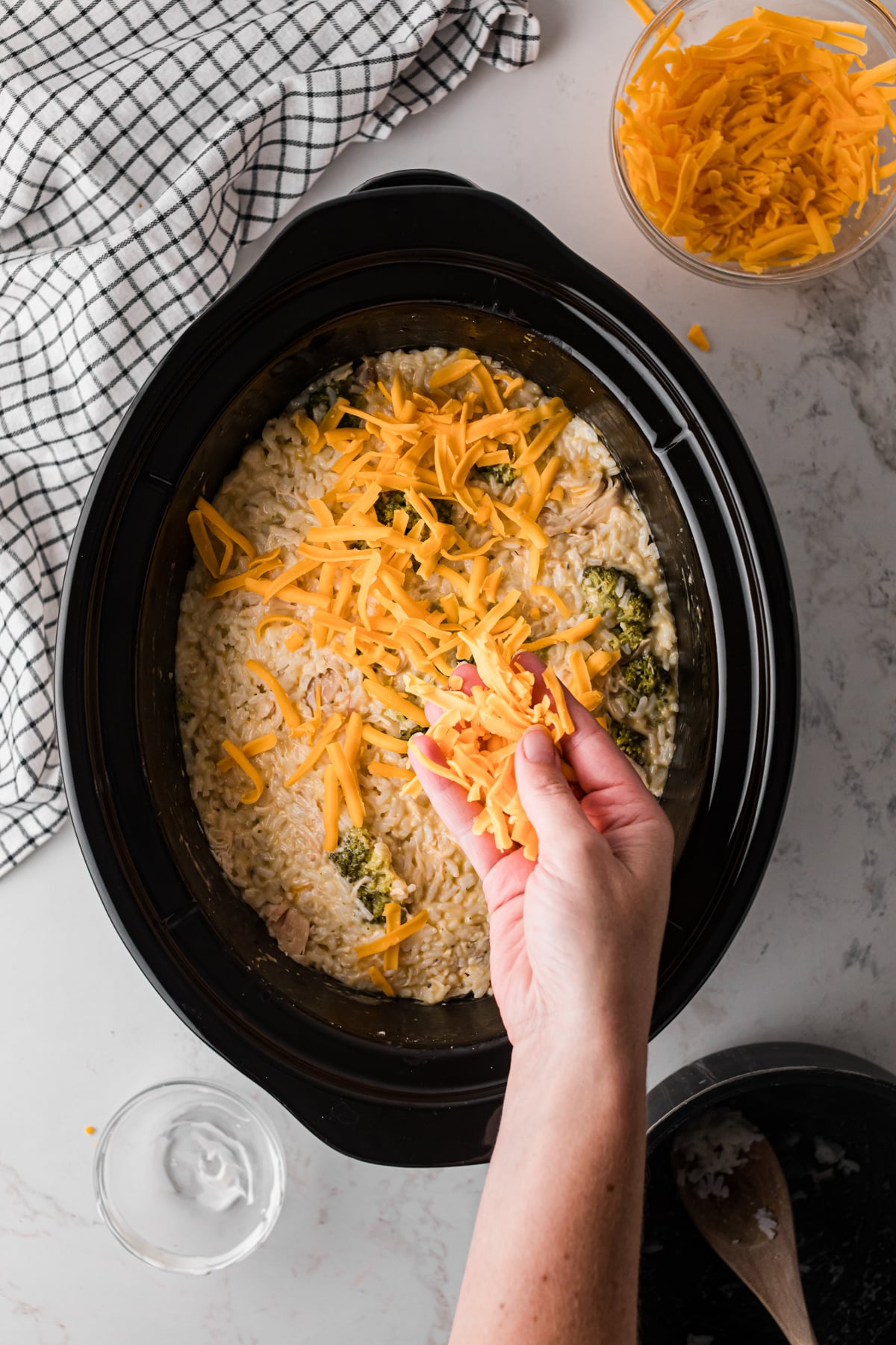 Sprinkling cheddar cheese on top of cooked chicken broccoli and rice in a crockpot.