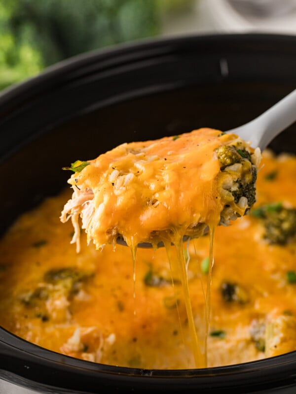 A large spoon with a scoop of chicken broccoli and rice being held over a crockpot.