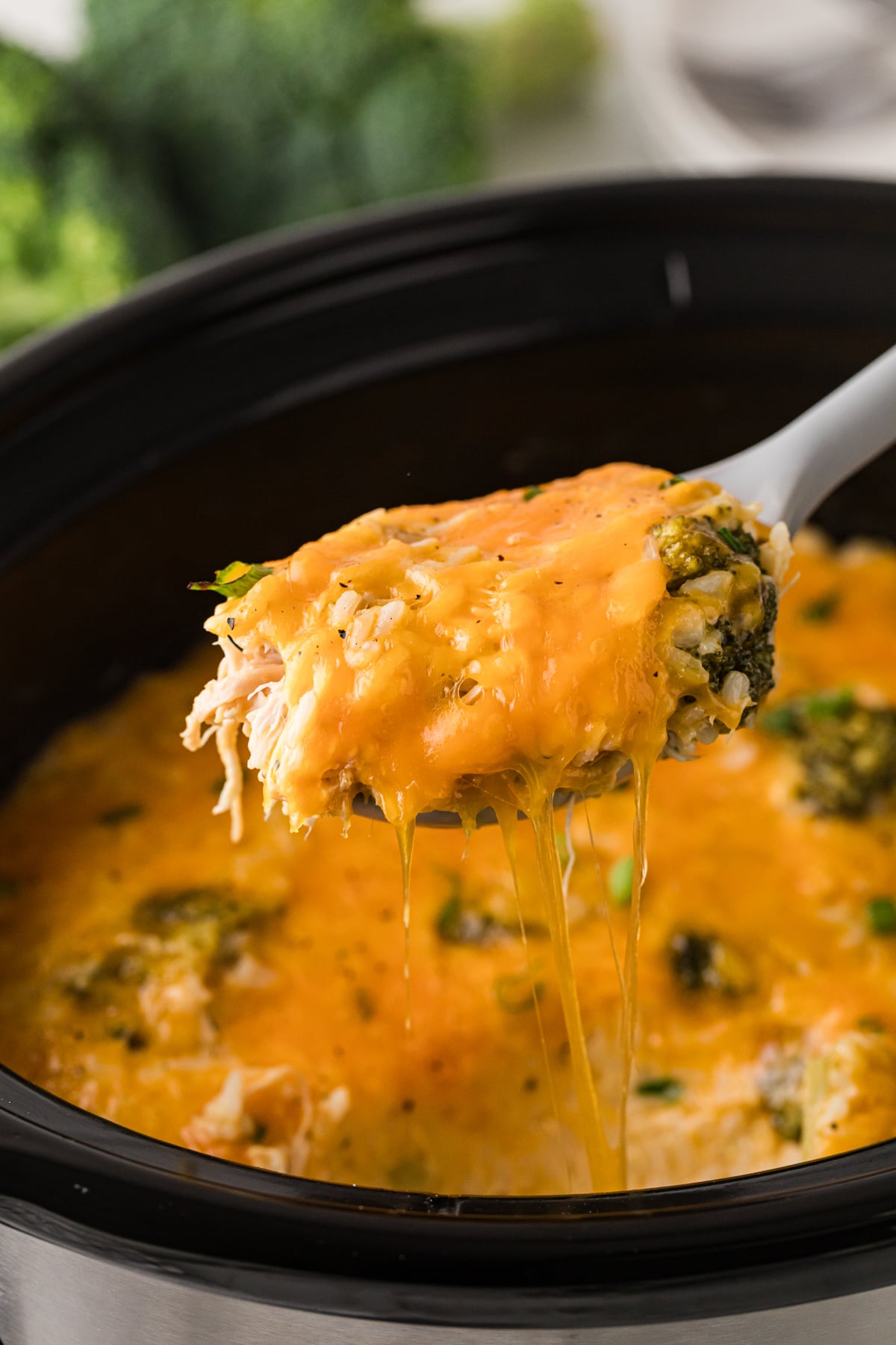 A large spoon with a scoop of chicken broccoli and rice being held over a crockpot.