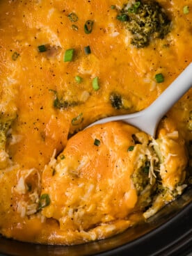 Chicken broccoli and rice in a slow cooker with a large spoon in it.