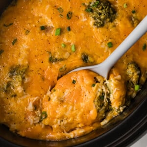 Chicken broccoli and rice in a slow cooker with a large spoon in it.