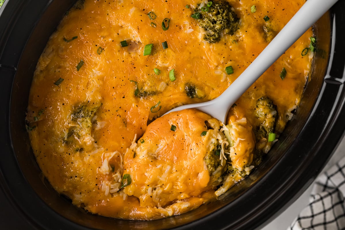 Chicken broccoli and rice in a slow cooker with a large spoon in it.