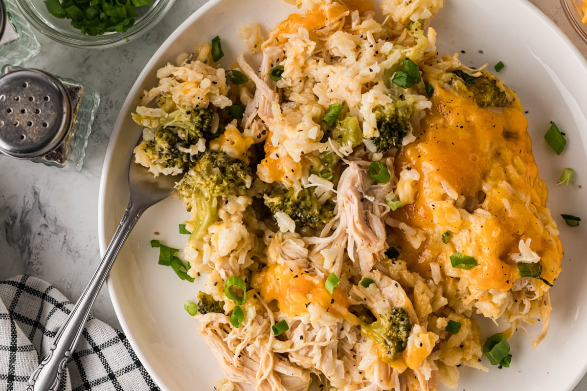 A serving of chicken with broccoli, rice, and melted cheddar cheese on a plate with a fork.