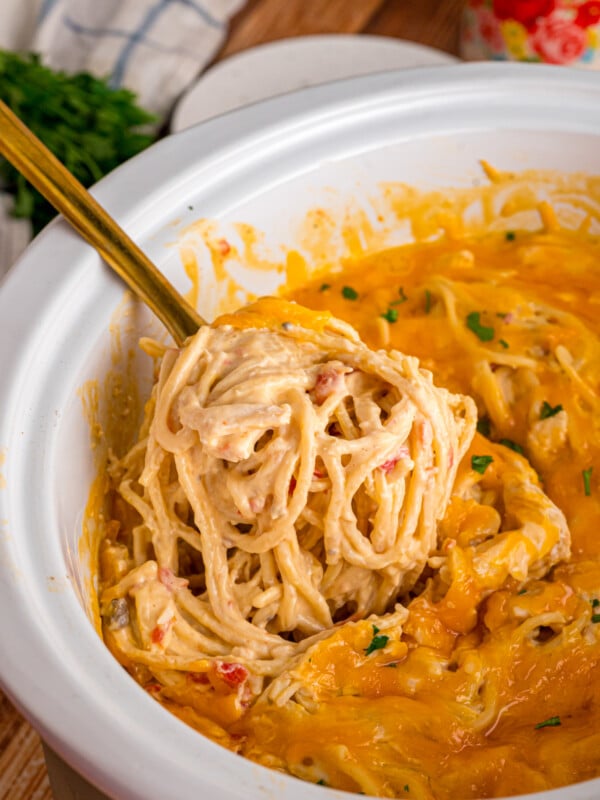 A spoon scooping spaghetti and chicken from a crockpot.