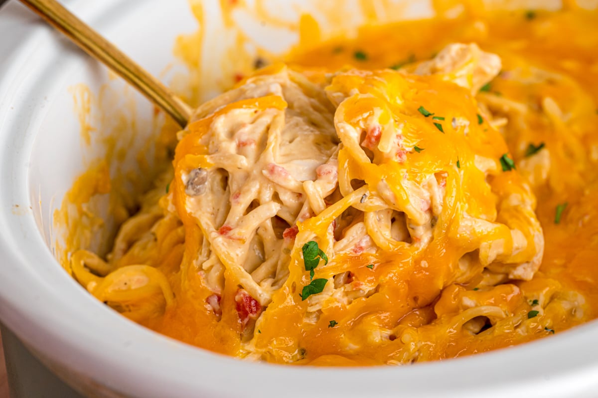 Chicken spaghetti in a crockpot with a spoon scooping some out.