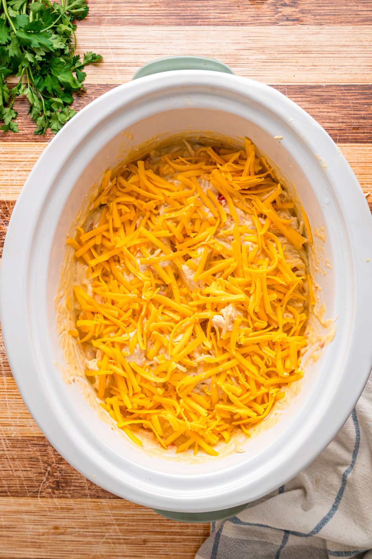 Cheddar cheese added on top of ingredients in a crockpot.