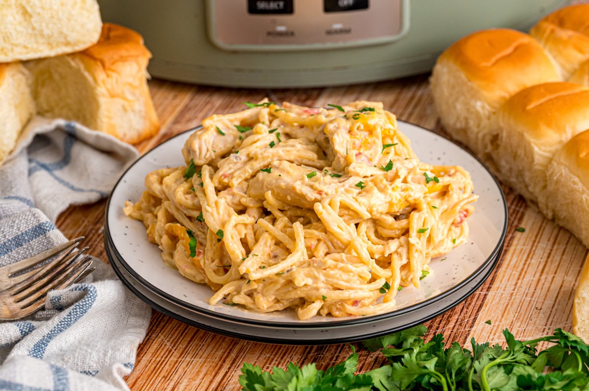 A plate of chicken spaghetti in front of a crockpot.