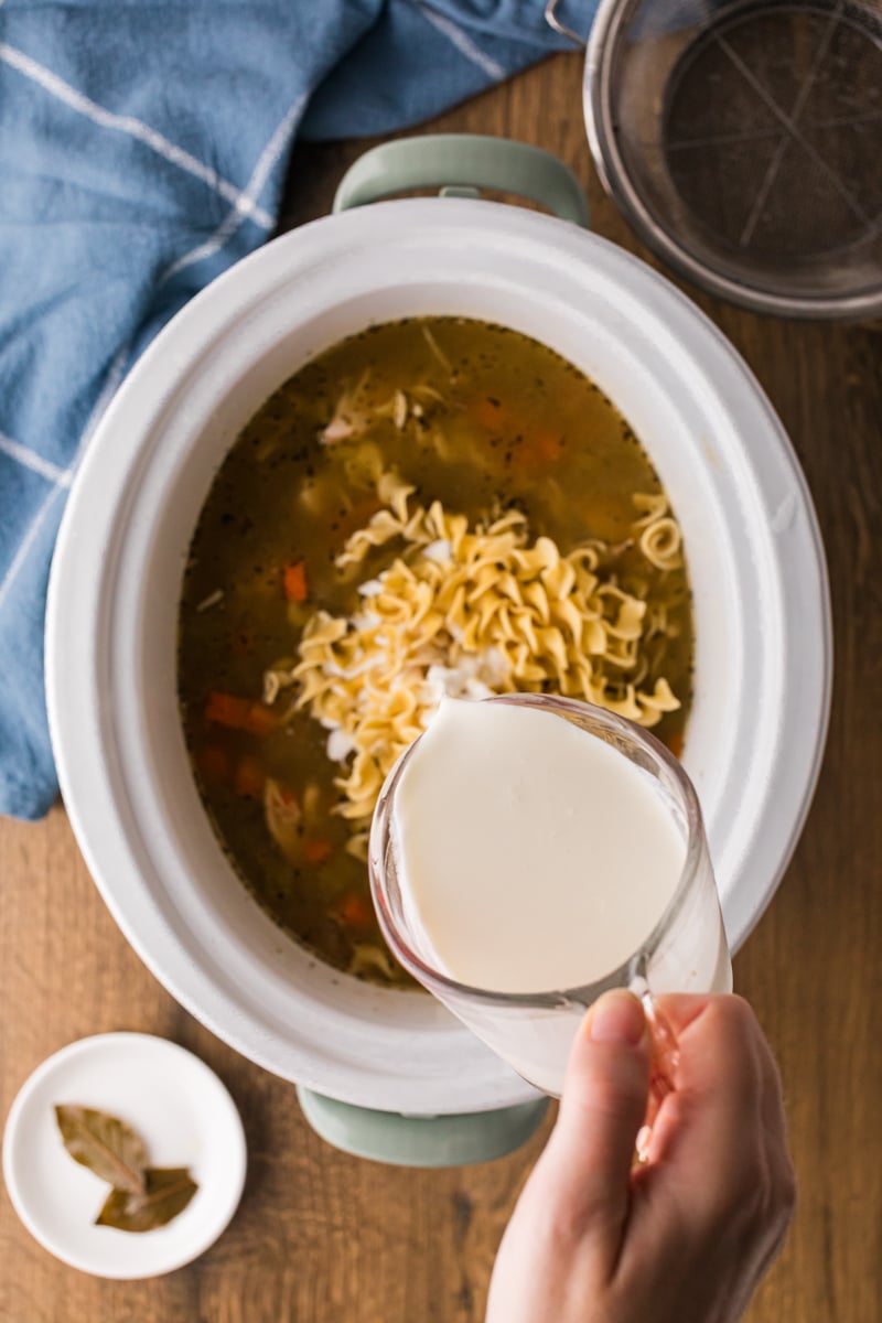 Heavy cream being poured into soup in a crockpot.