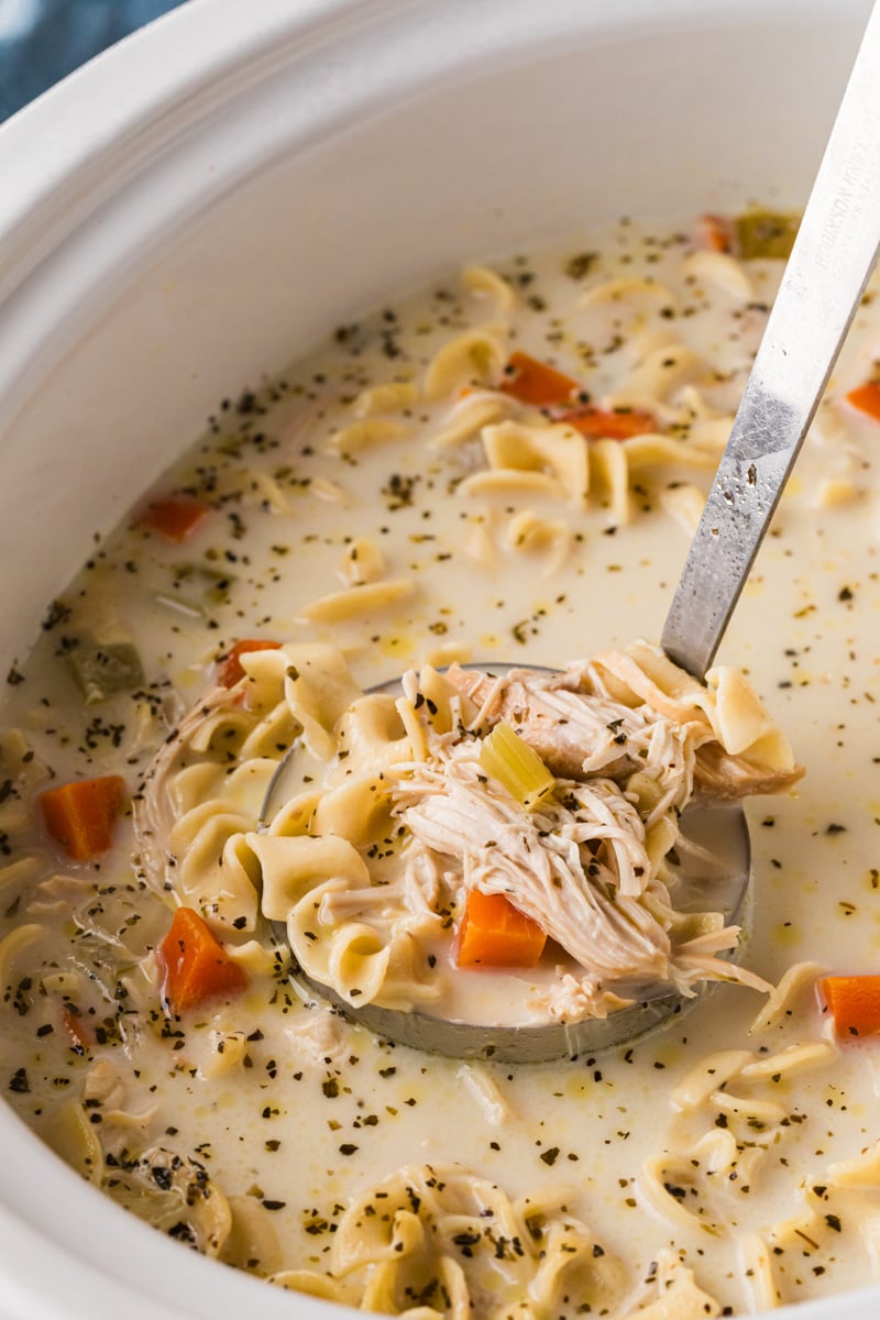 A ladle full of creamy chicken noodle soup coming out of a crockpot.