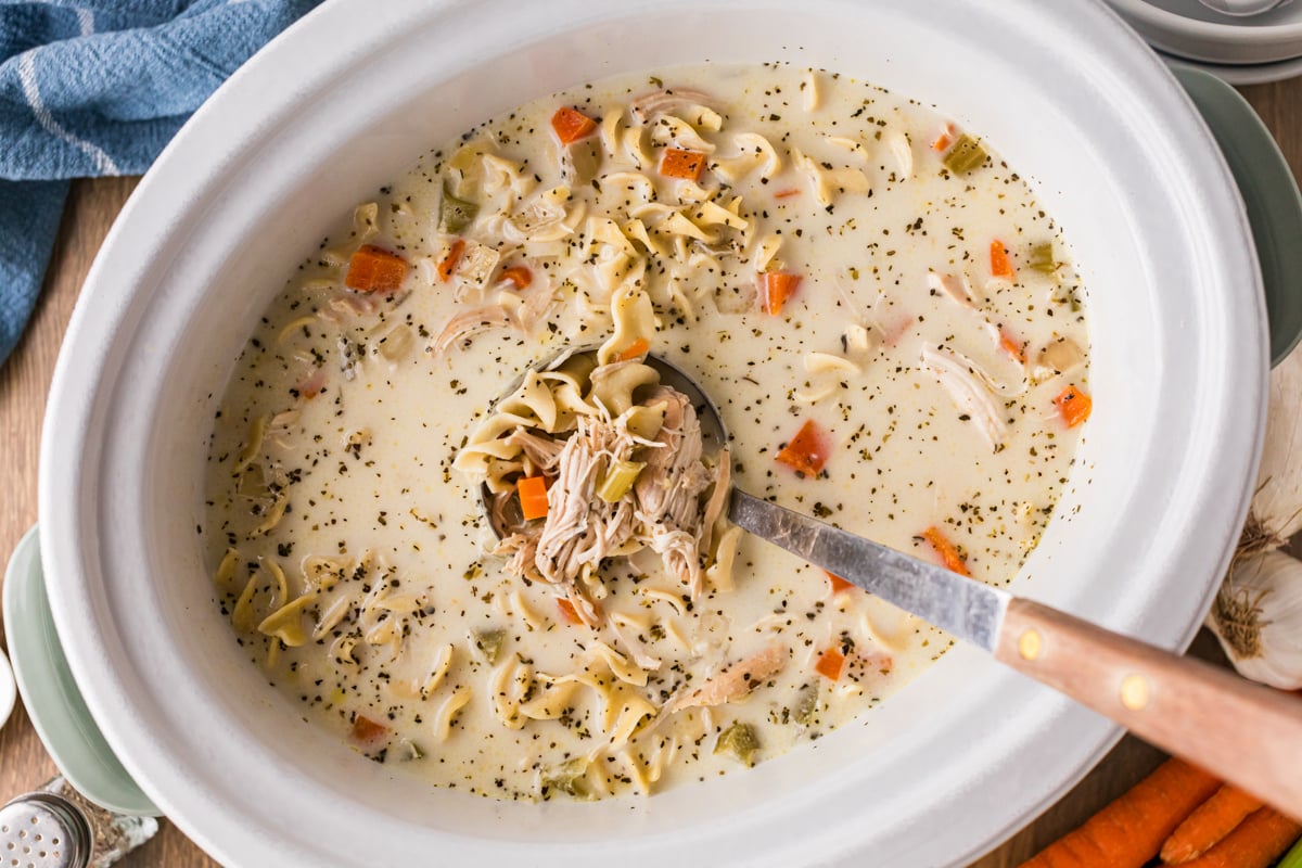Chicken noodle soup with cream in a crockpot with a ladle.