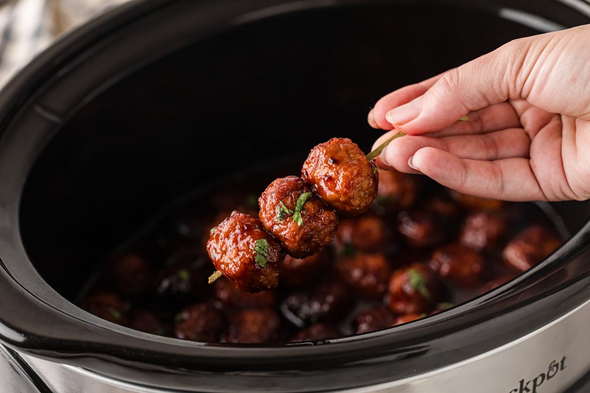 Holding 3 meatballs on a stick over a crockpot.