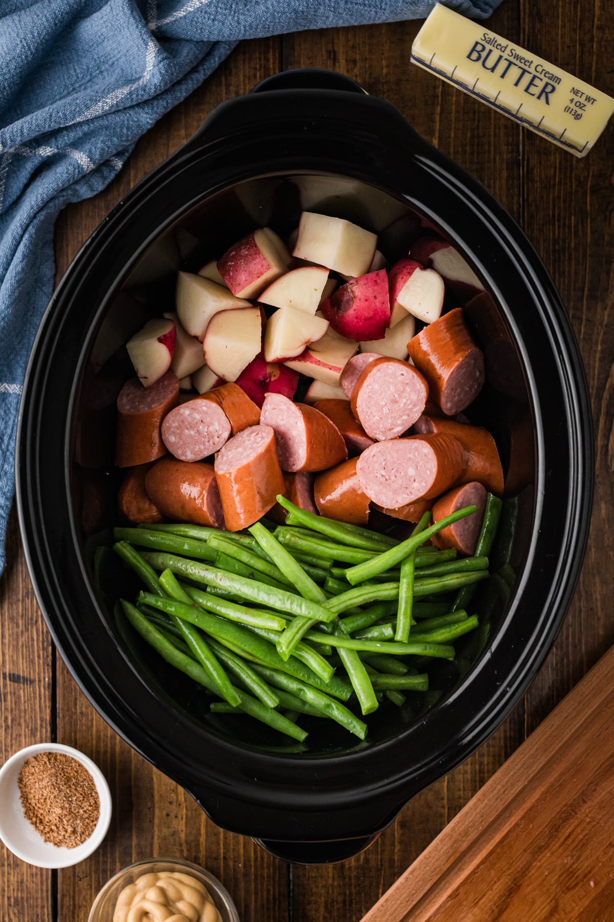 Potatoes, kielbasa, and green beans arranged separately in a crockpot.