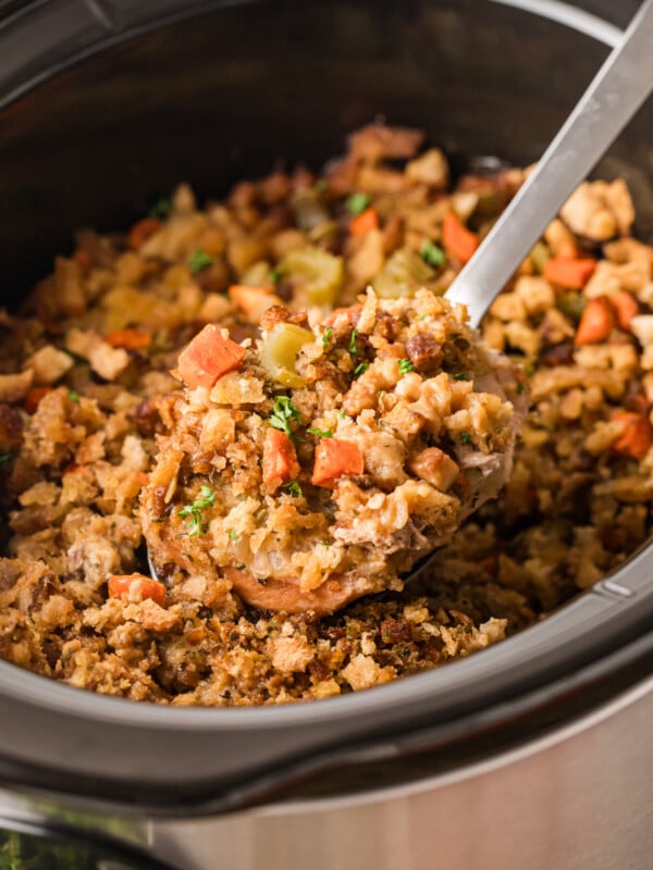 Pork chops and stuffing in a crockpot after cooking with a large spoon scooping some out.