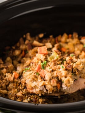 A large metal spoon holding a pork chop with stuffing over a crockpot.