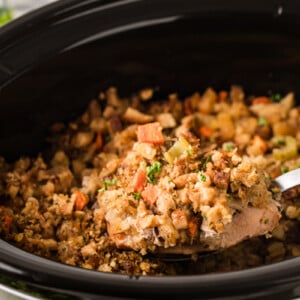 A large metal spoon holding a pork chop with stuffing over a crockpot.