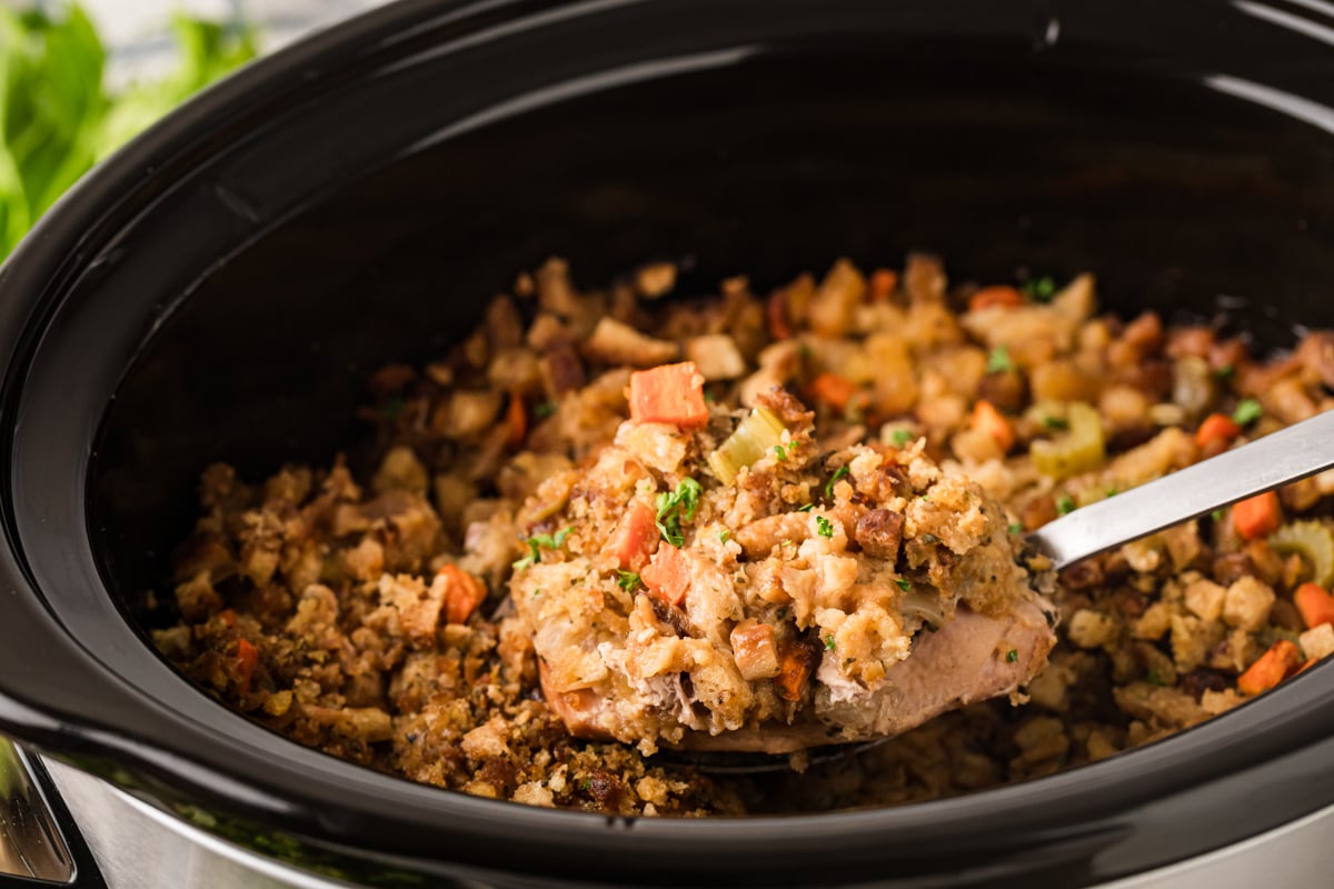 A large metal spoon holding a pork chop with stuffing over a crockpot.