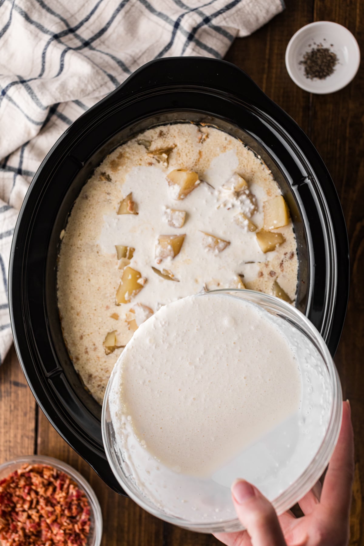 Pouring heavy cream and flour mixture into a crockpot of cooked ingredients.