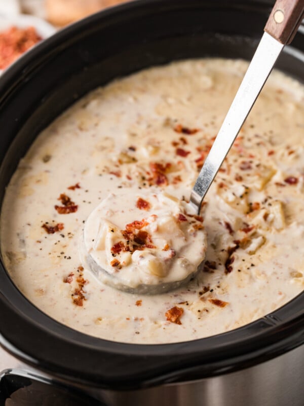 A ladle holding a scoop of potato bacon soup over a crockpot.