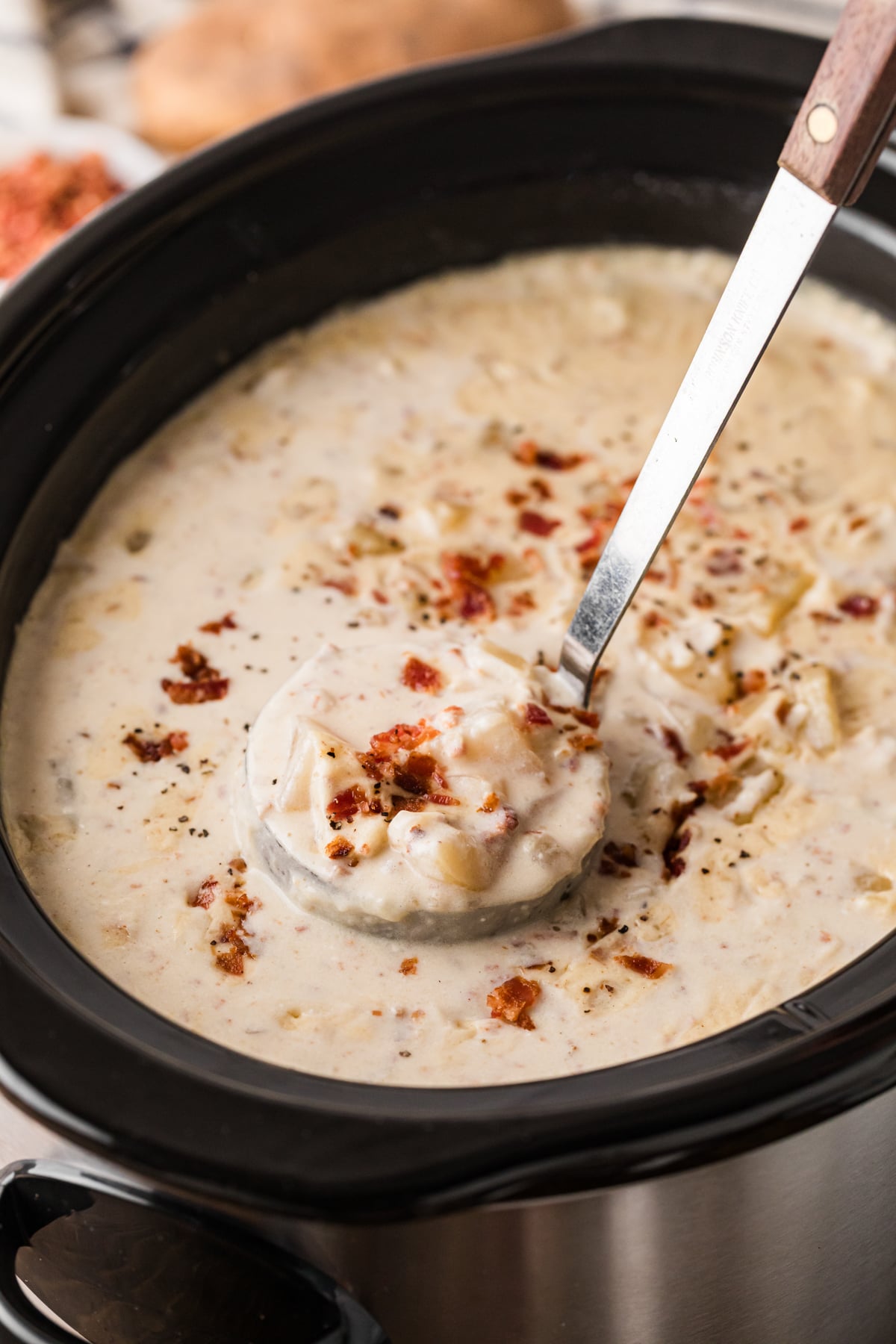 A ladle holding a scoop of potato bacon soup over a crockpot.