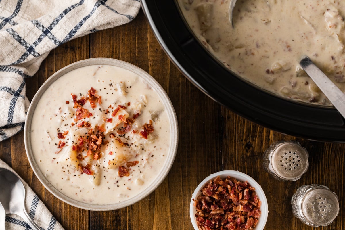 A bowl of potato bacon soup next to a crockpot.