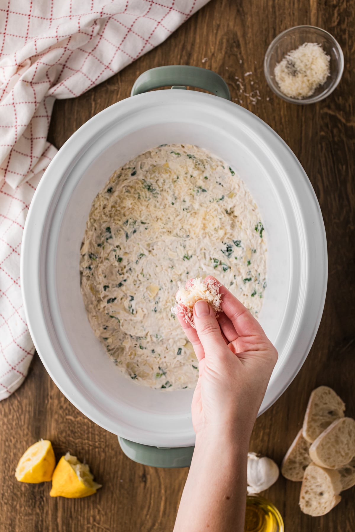 Sprinkling parmesan cheese on top of dip in a slow cooker.