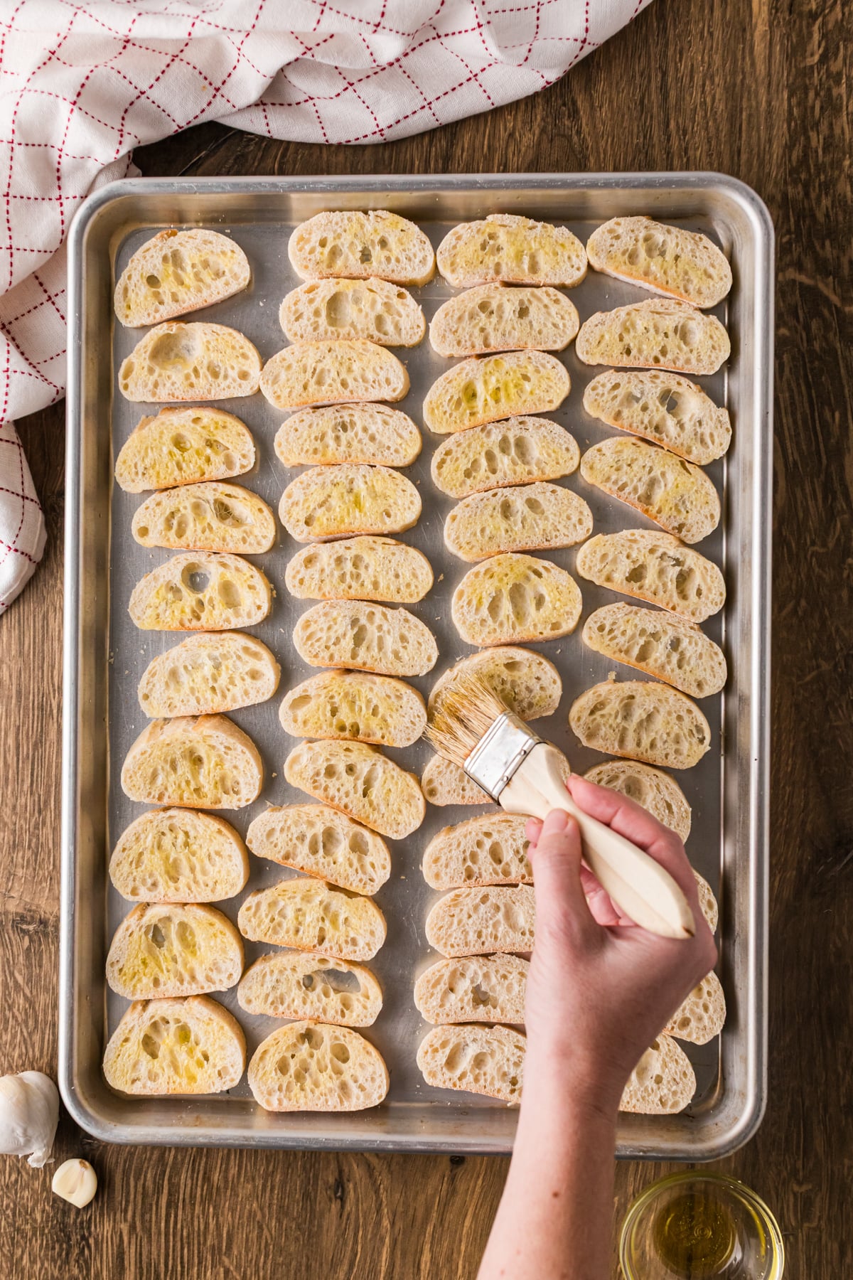 Coating baguette pieces on a baking sheet with olive oil using a pastry brush.