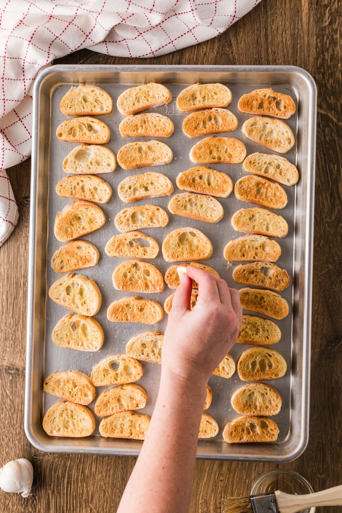 Rubbing garlic over baked baguette slices on a sheet pan.