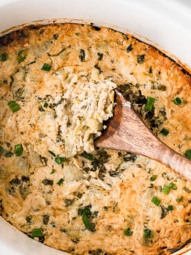 A crockpot filled with crab spinach artichoke dip with a wooden spoon in it.