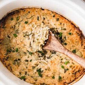 A crockpot filled with crab spinach artichoke dip with a wooden spoon in it.