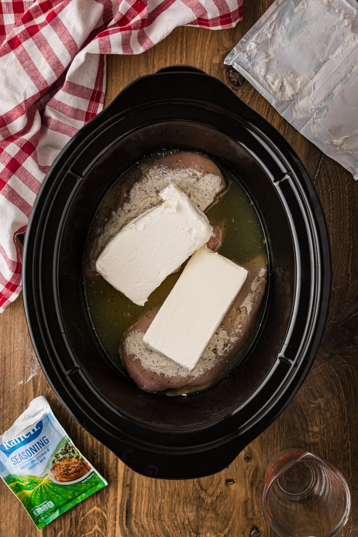 Seasoned chicken breasts with broth and cream cheese in a crockpot.