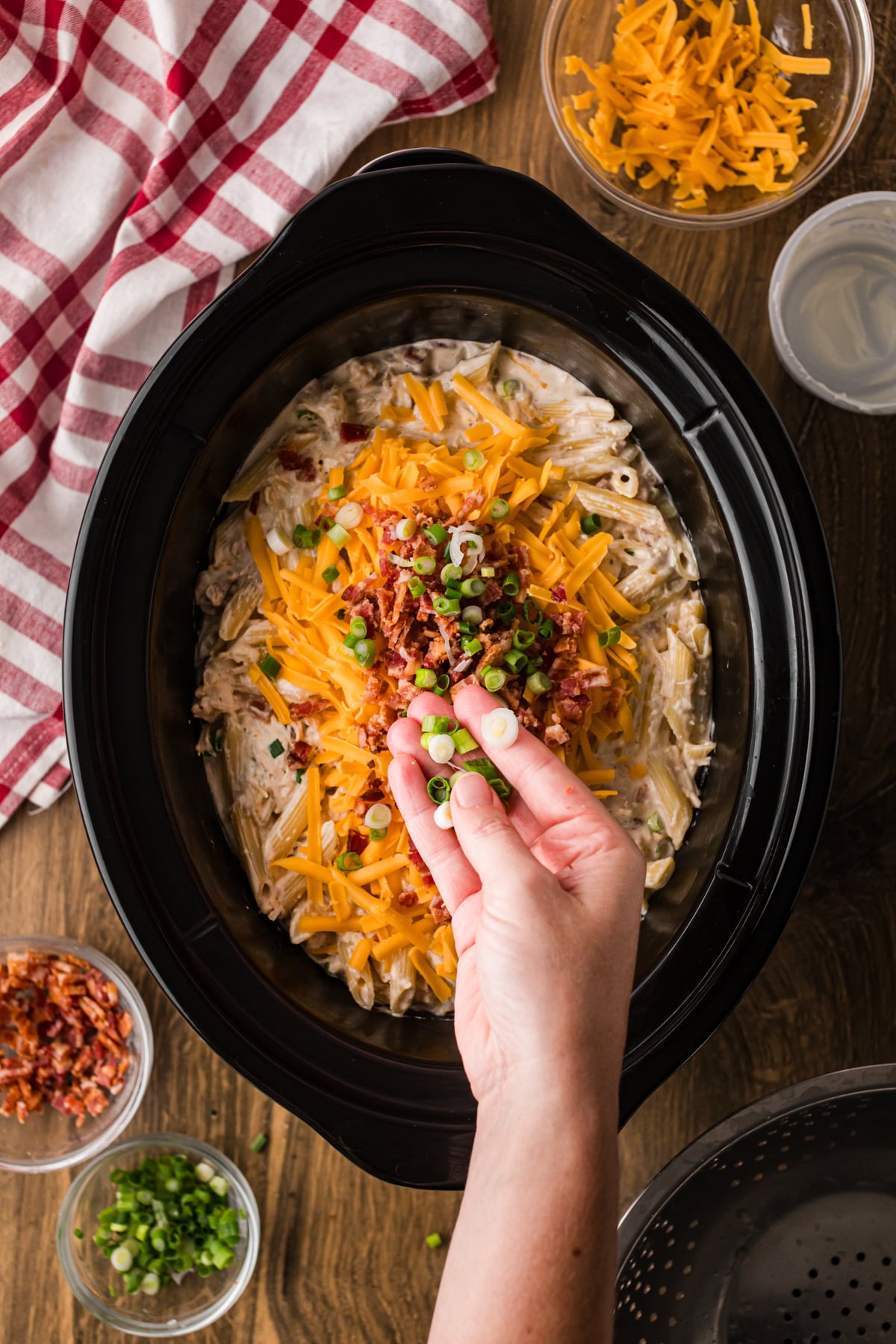 Sprinkling green onions over top of pasta and chicken in a crockpot.