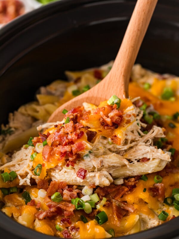 Crack chicken pasta in a slow cooker with a wooden spoon scooping some out.