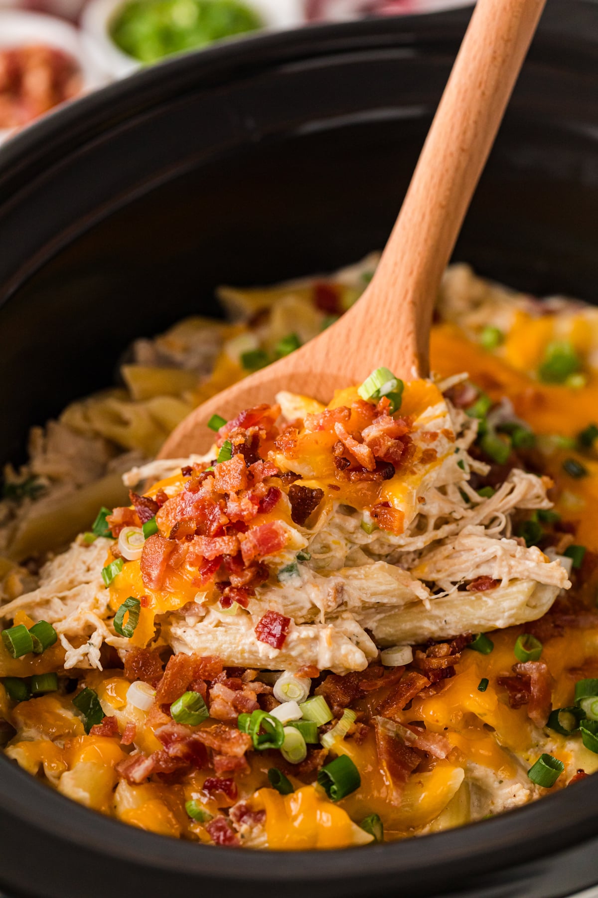 Crack chicken pasta in a slow cooker with a wooden spoon scooping some out.