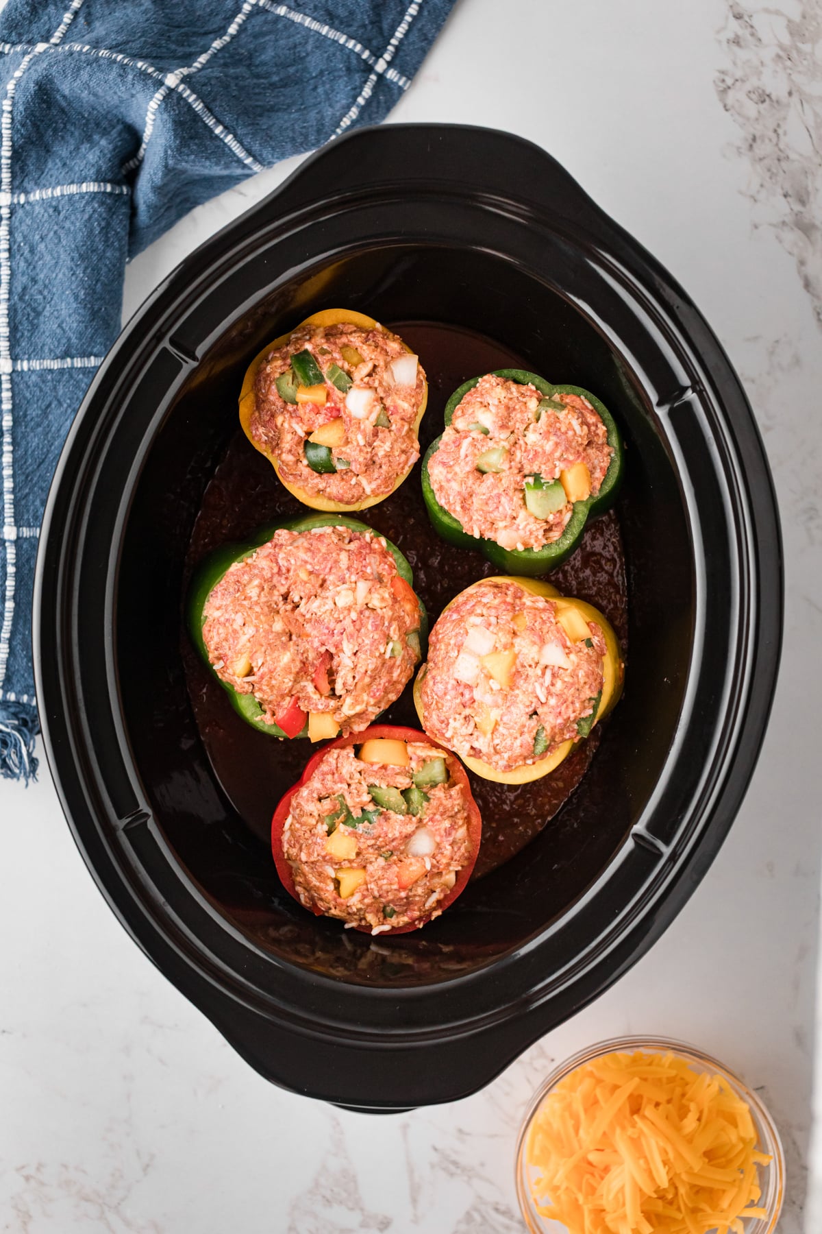 Uncooked stuffed bell peppers on a layer of salsa in a crockpot.