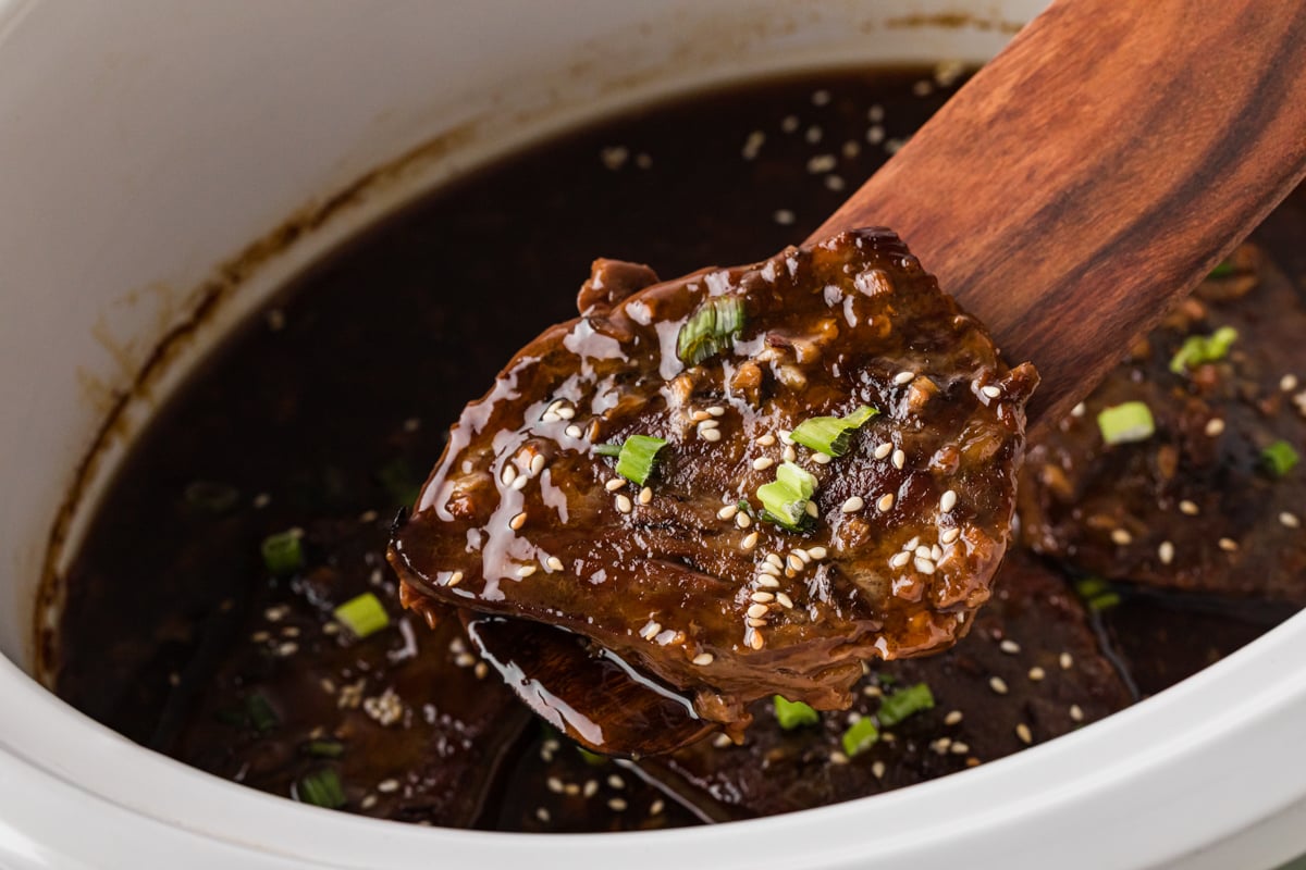 A wooden utensil grabbing a piece of teriyaki steak from a crockpot.