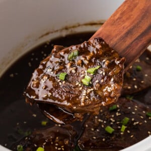 Lifting a teriyaki steak from a crockpot with a wooden utensil.