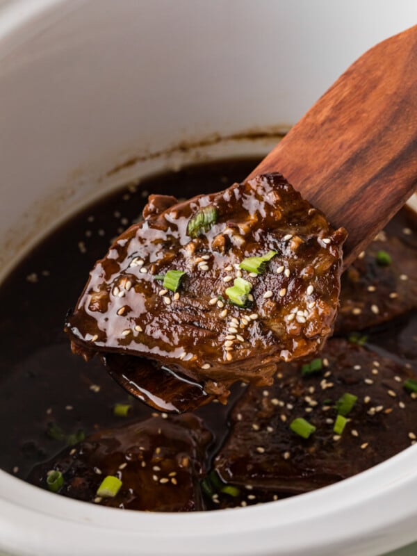 Lifting a teriyaki steak from a crockpot with a wooden utensil.
