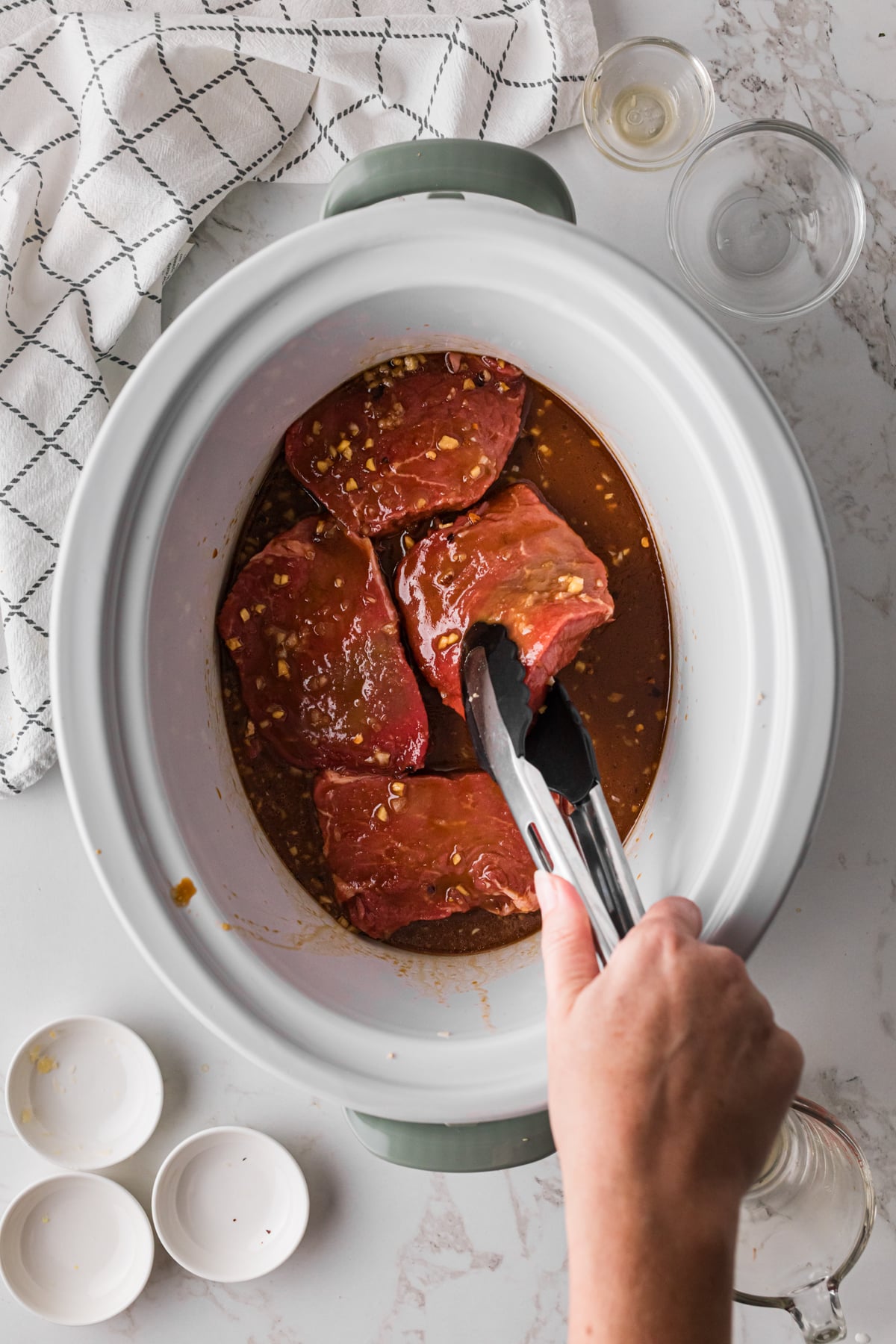 Using tongs to flip steaks over in a marinade mixture in a crockpot.