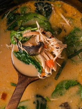 A ladle holding a scoop of curry soup over a crockpot.