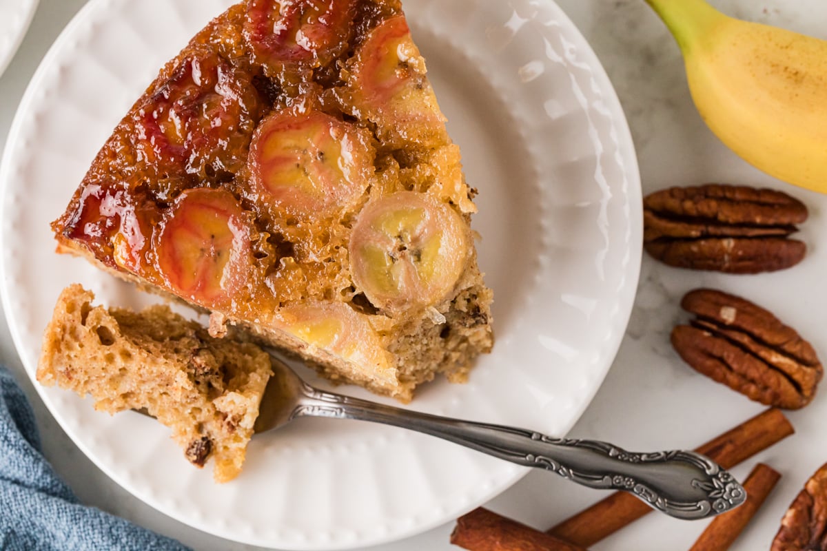 A slice of banana upside down cake with a fork cutting a bite.