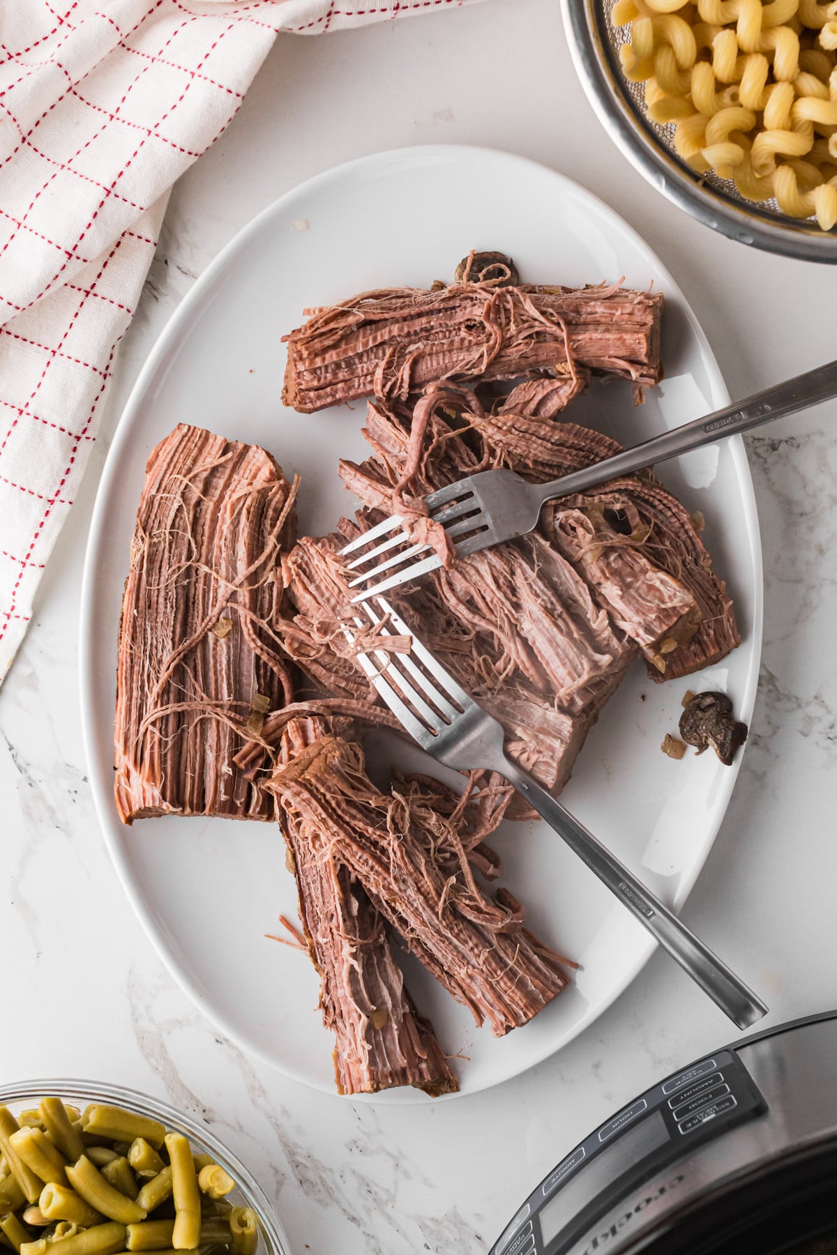 Shredding cooked beef roast on a plate with two forks.