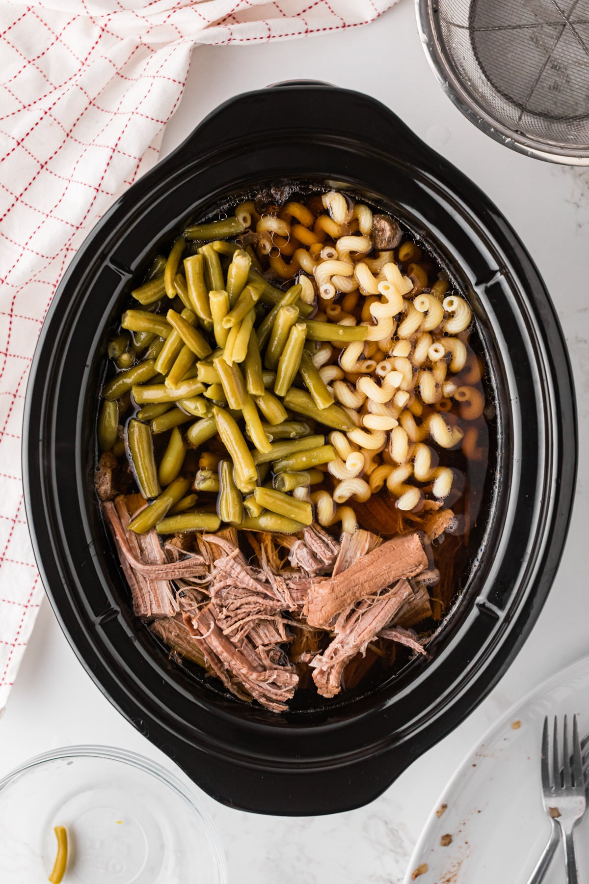 Shredded beef, pasta, and green beans added to a crockpot with cooked mushrooms, onions, and broth.