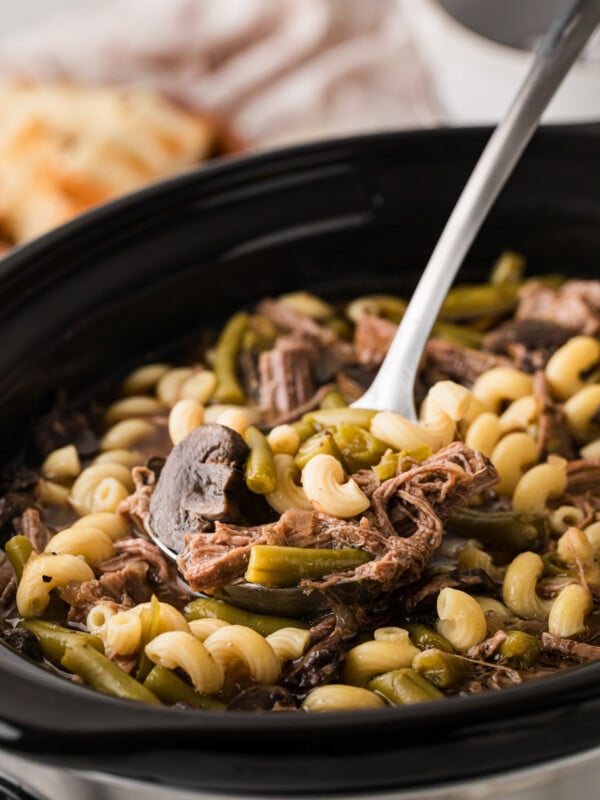 A ladle with a scoop of french dip soup in it coming out of a crockpot.