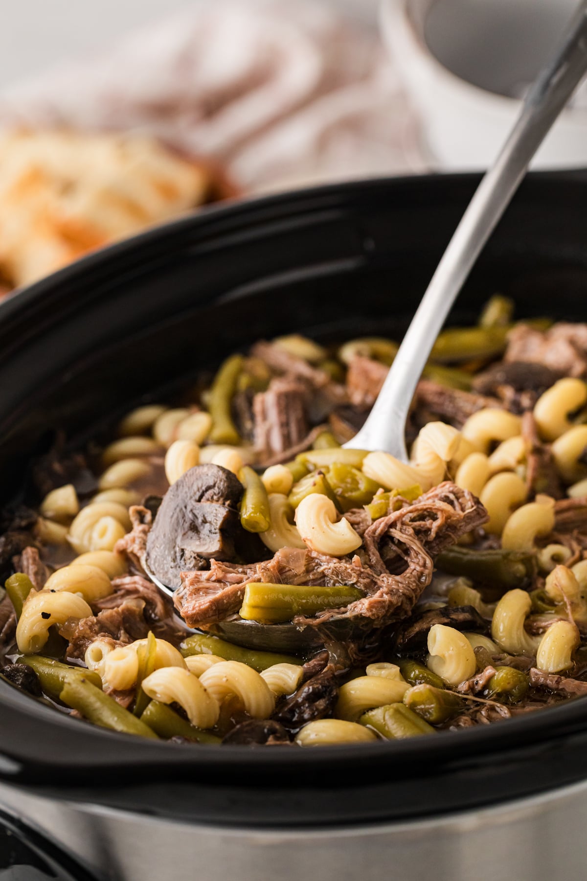 A ladle with a scoop of french dip soup in it coming out of a crockpot.
