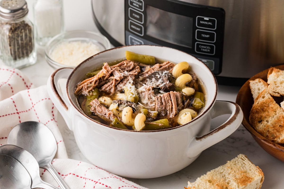 A bowl of french dip soup in front of a crockpot.