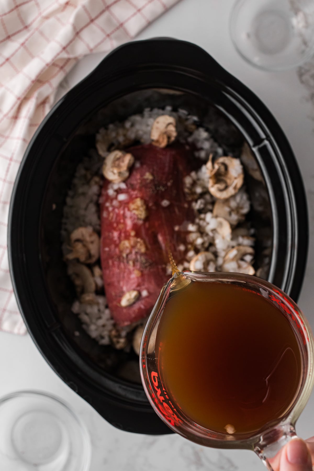 Pouring beef broth onto ingredients in a crockpot.