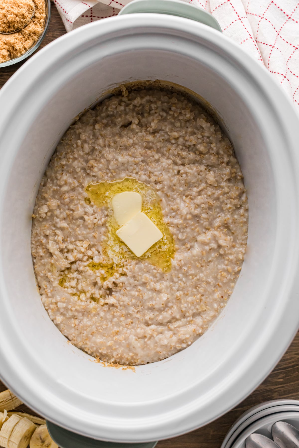 Oatmeal in a slow cooker with two pats of butter.